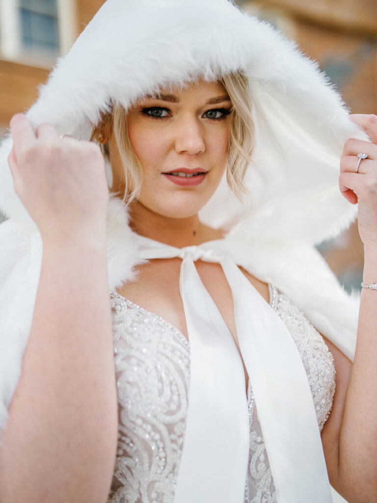A bride with a cape in front of Sun Valley Lodge in the snow before wedding.